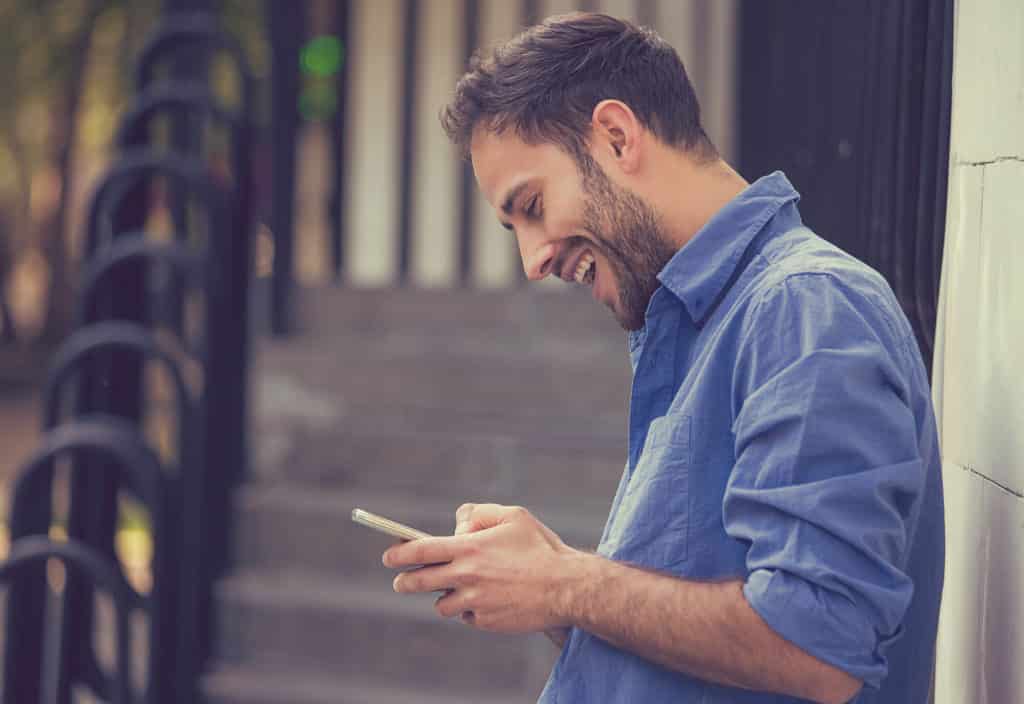 A man is smiling while using his cell phone for social media management.