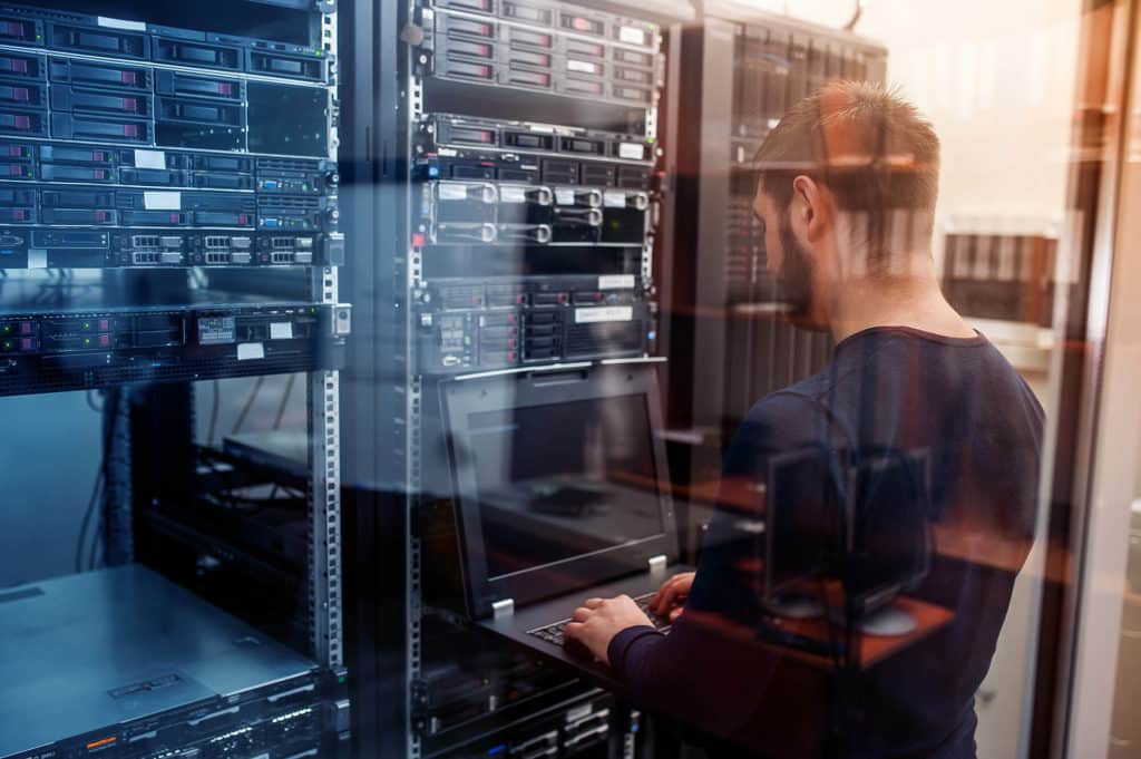 A man providing IT services working on a laptop in a server room.