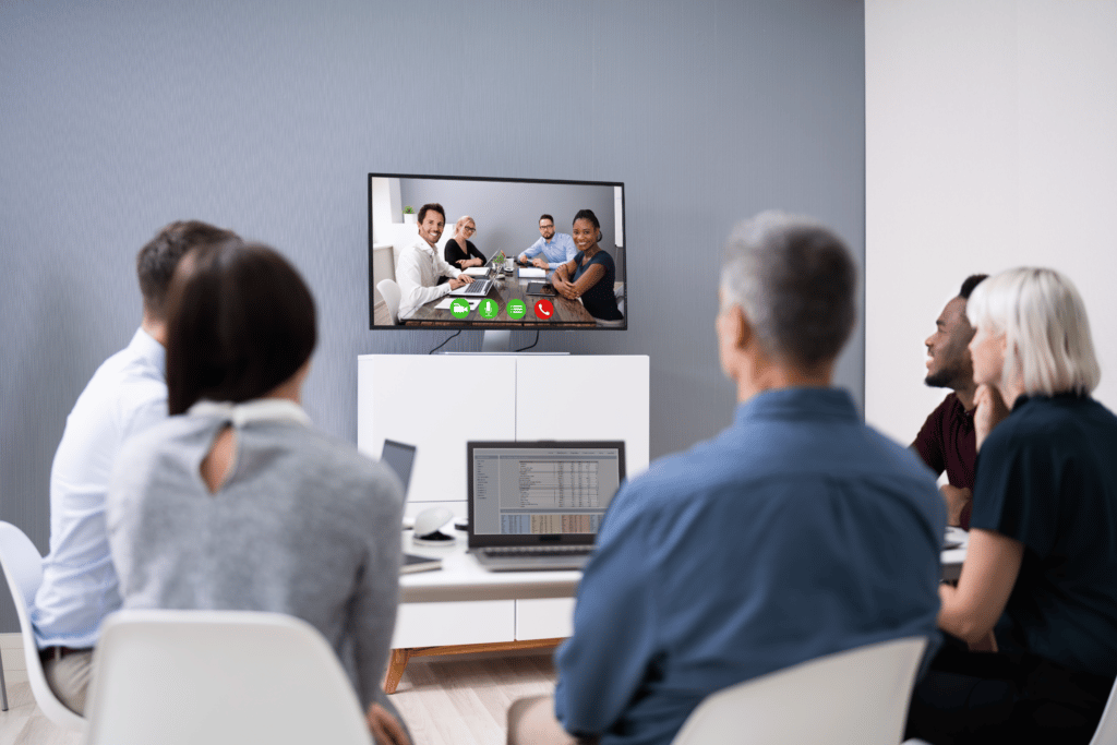 A group of people using computer help services sitting around a table watching a video conference.